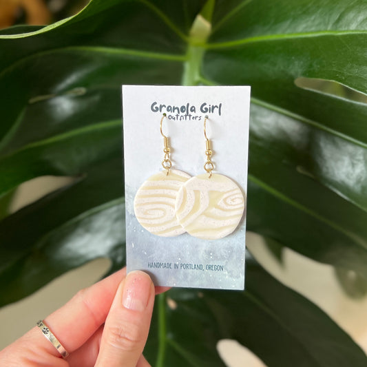 Handmade earrings on a 'Granola Girl Outfitters' card held in front of green leaves.