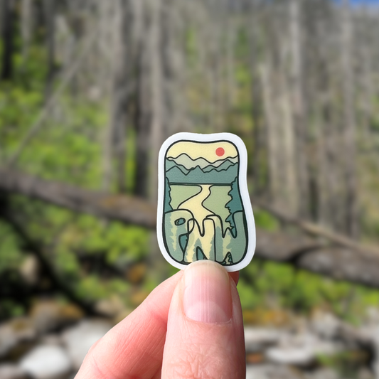 Hand holding a nature-themed sticker with a blurred forest background