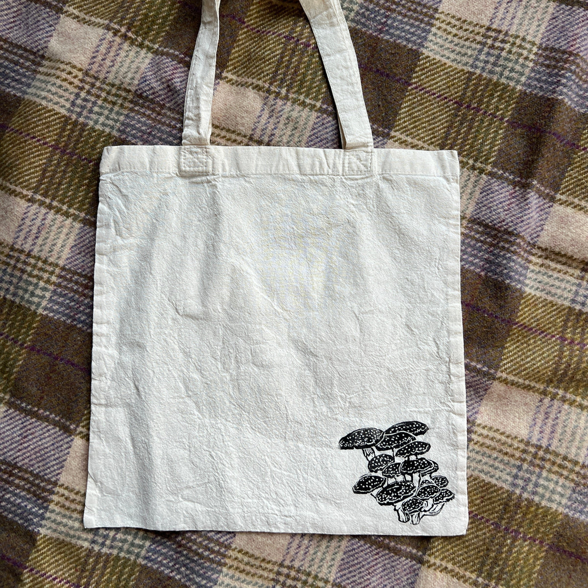 White tote bag with mushroom design on a plaid fabric background