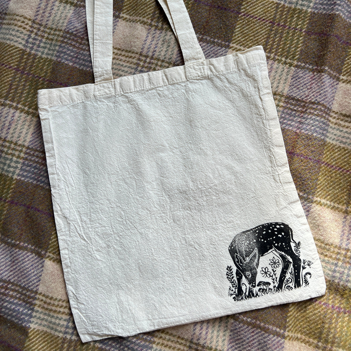 White tote bag with a black and white design of a deer on a plaid fabric background