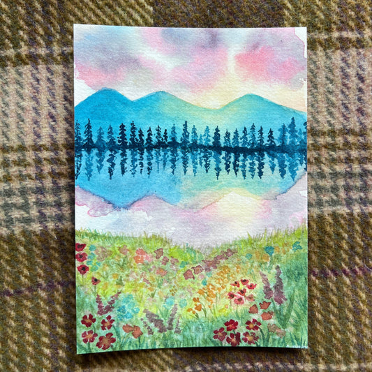 watercolor of a meadow looking over a lake with mountains and pine trees