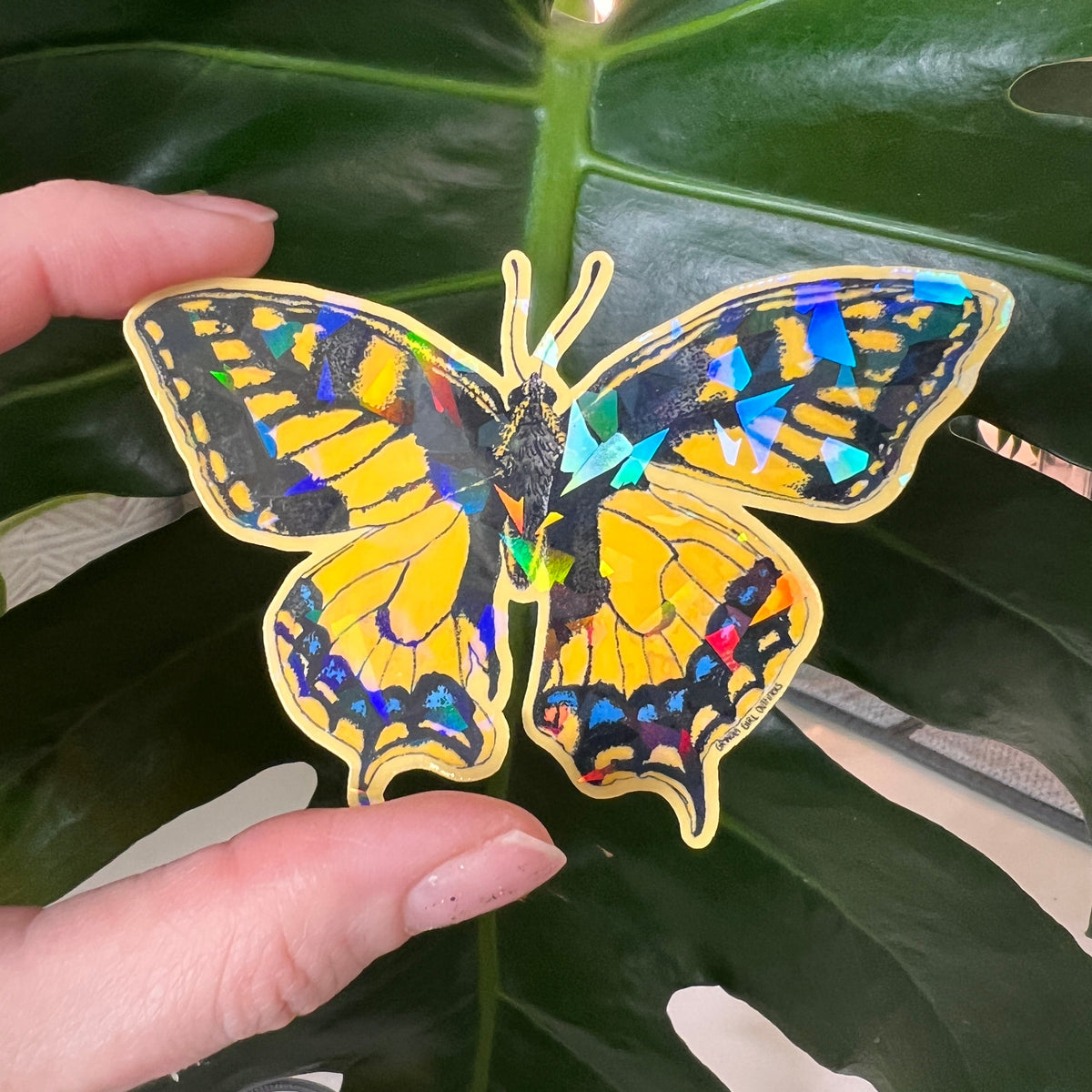 Holographic butterfly sticker held over a leafy green background