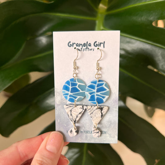 Earrings on a 'Granola Girl' branded card held in front of green leaves.