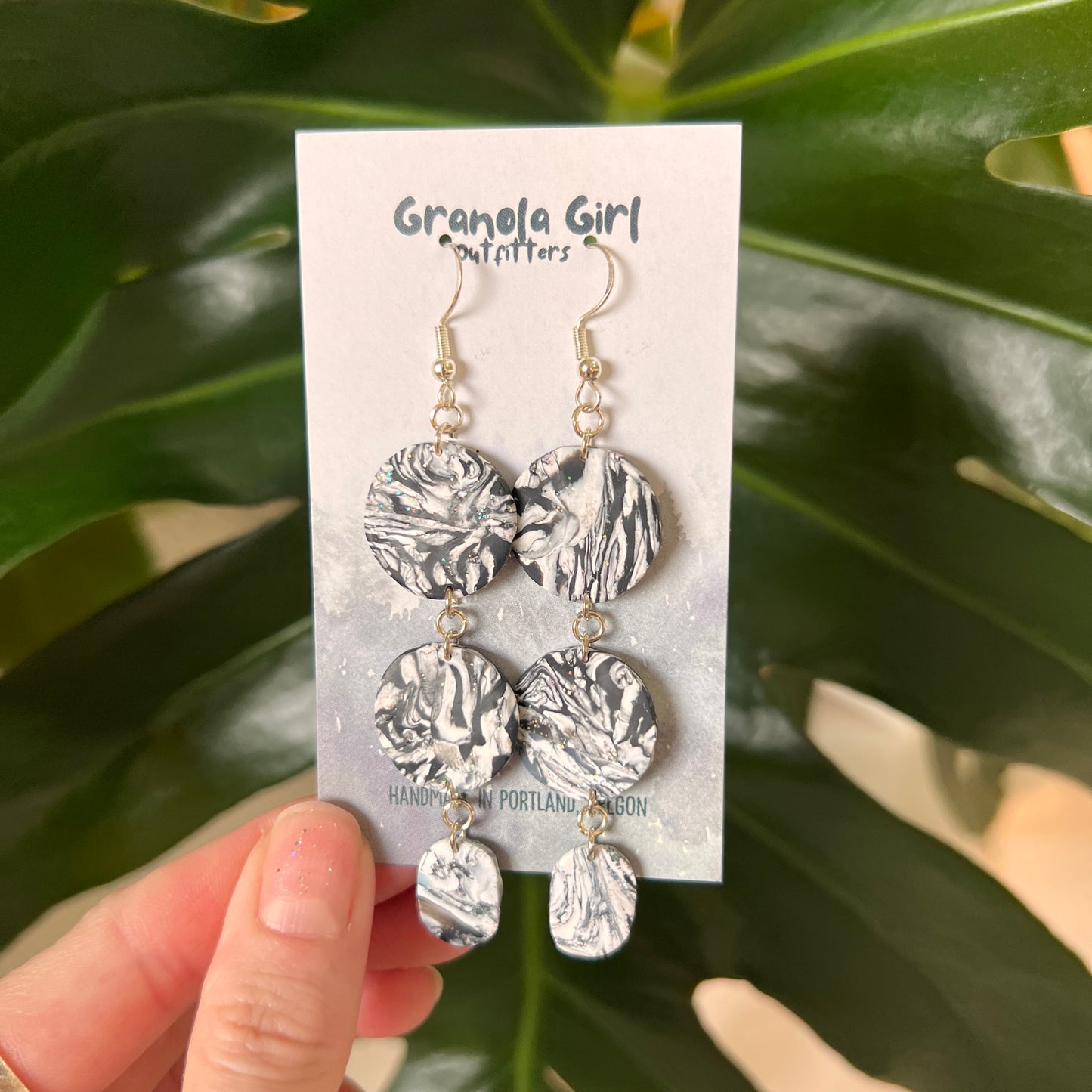Silver earrings on a 'Granola Girl' branded card held against a green leafy background