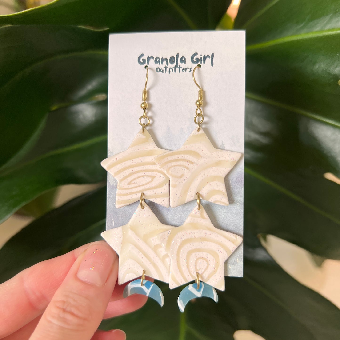 Star-shaped earrings on a 'Granola Girl Outfitters' card held against a green leafy background.
