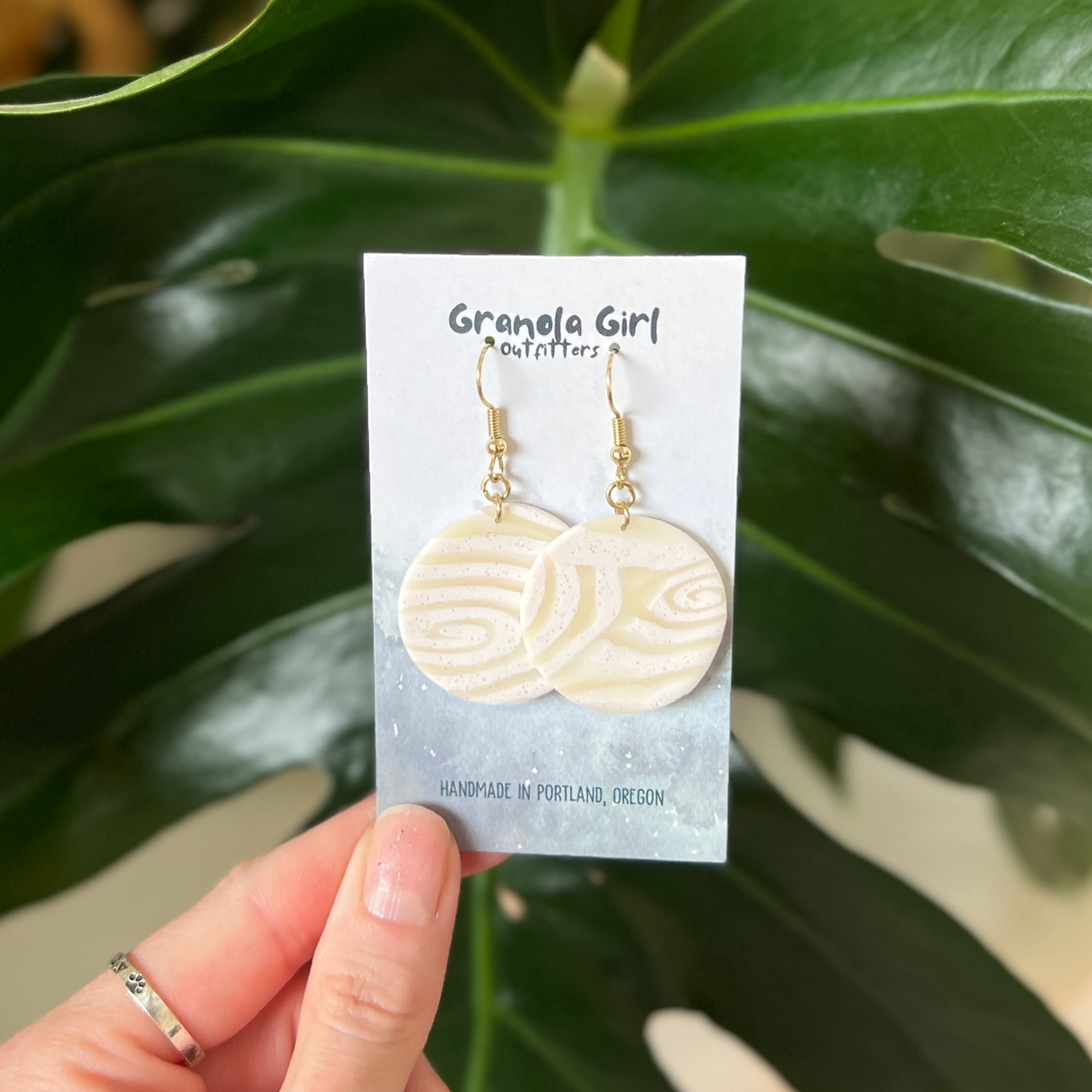 Handmade earrings on a 'Granola Girl Outfitters' card held in front of green leaves.