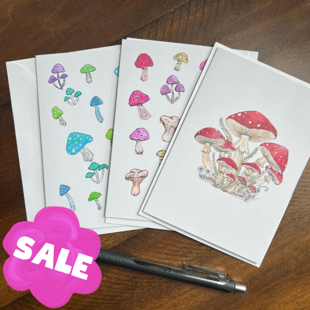 set of mushroom greeting cards on a wooden surface with a pen and a "sale" sign