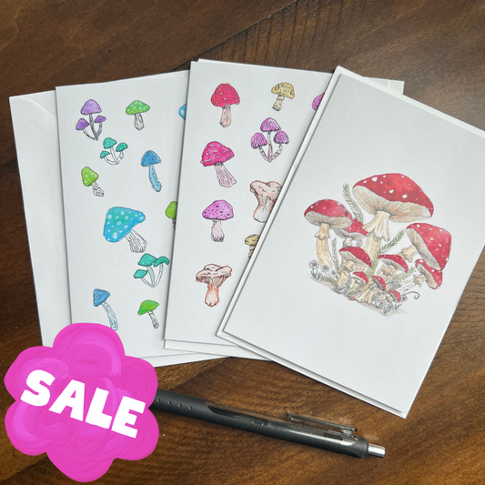 set of mushroom greeting cards on a wooden surface with a pen and a "sale" sign