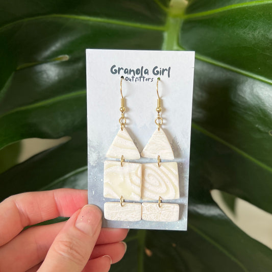 White triangle earrings on a 'Granola Girl Outfitters' card held against a green leafy background