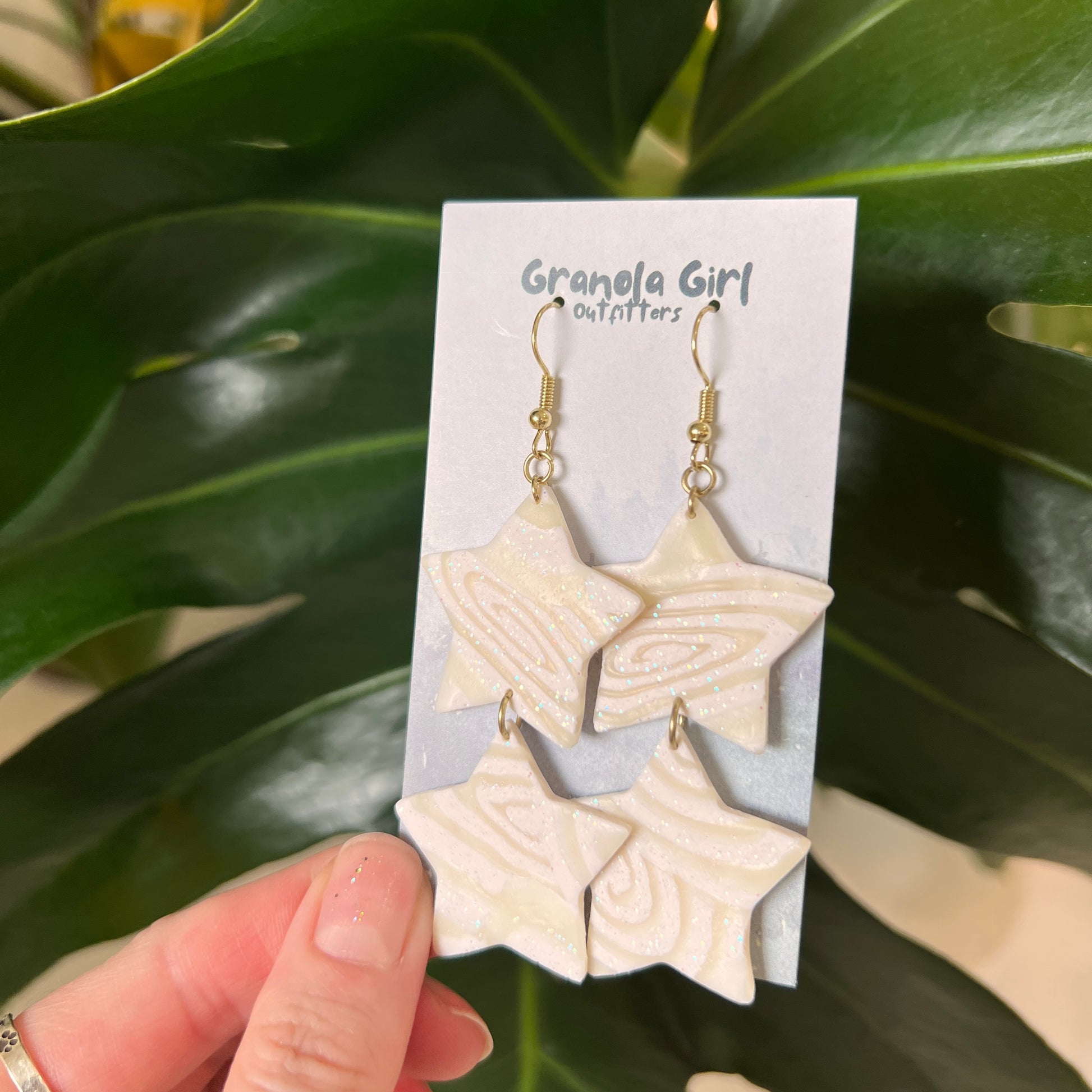 Star-shaped earrings on a 'Granola Girl Outfitters' card held against a green leafy background.