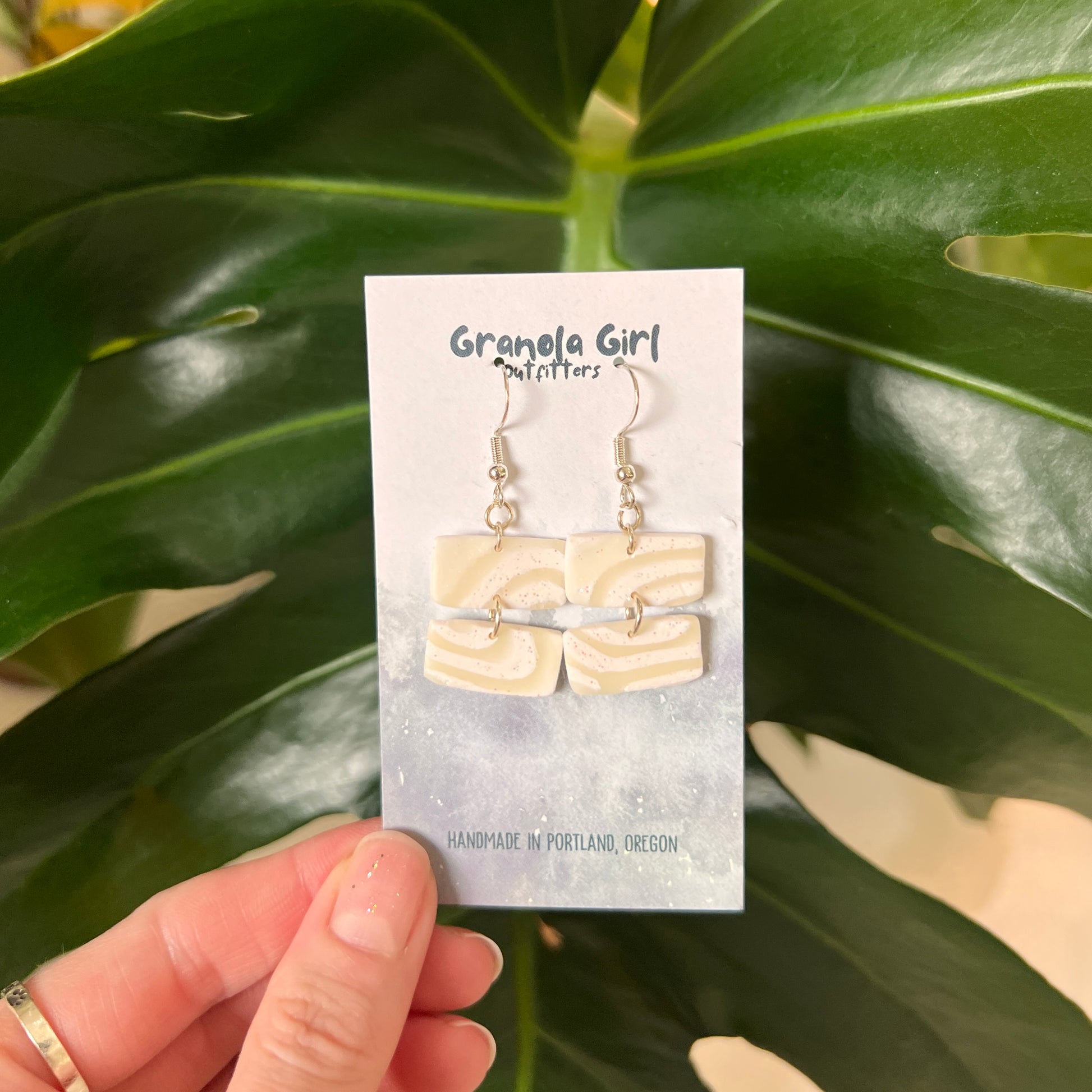 Earrings on a 'Granola Girl' branded card held against a green leafy background