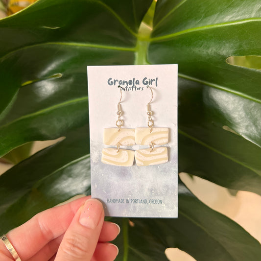 Earrings on a 'Granola Girl' branded card held against a green leafy background