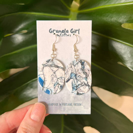 Earrings on a 'Granola Girl Outfitters' card held against a leafy green background