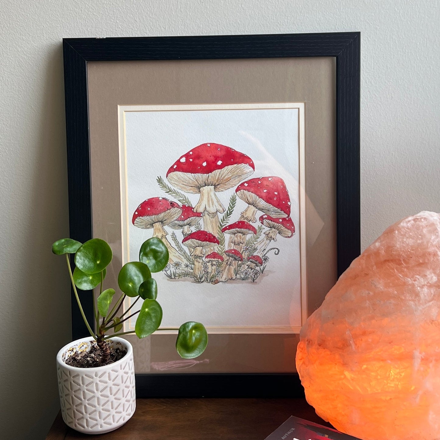 Framed artwork of mushrooms on a wall next to a potted plant and glowing crystal lamp.