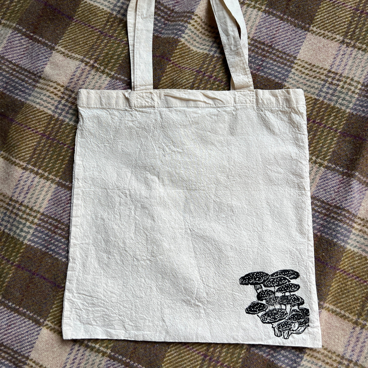 White tote bag with mushroom design on a plaid fabric background