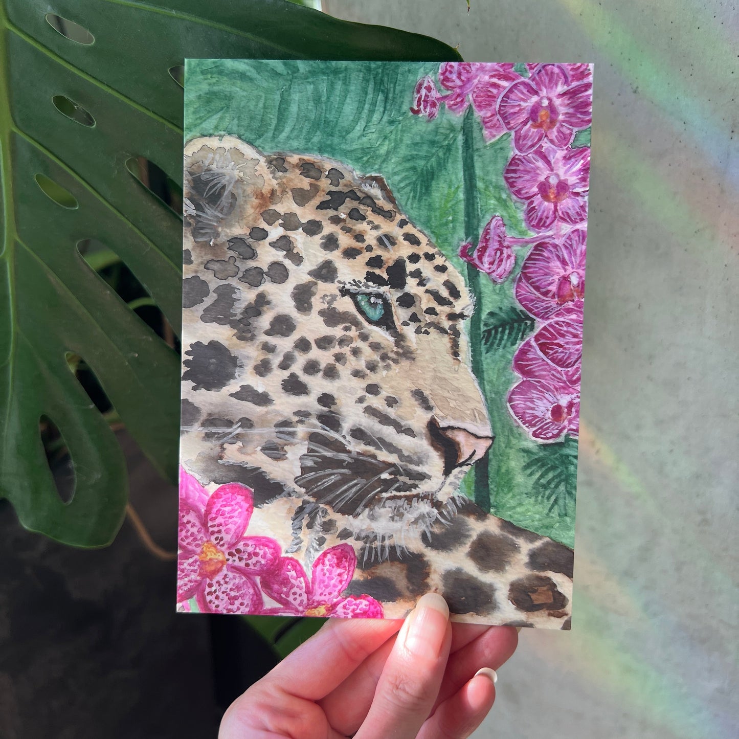 Hand holding a art print with a leopard design against a floral background